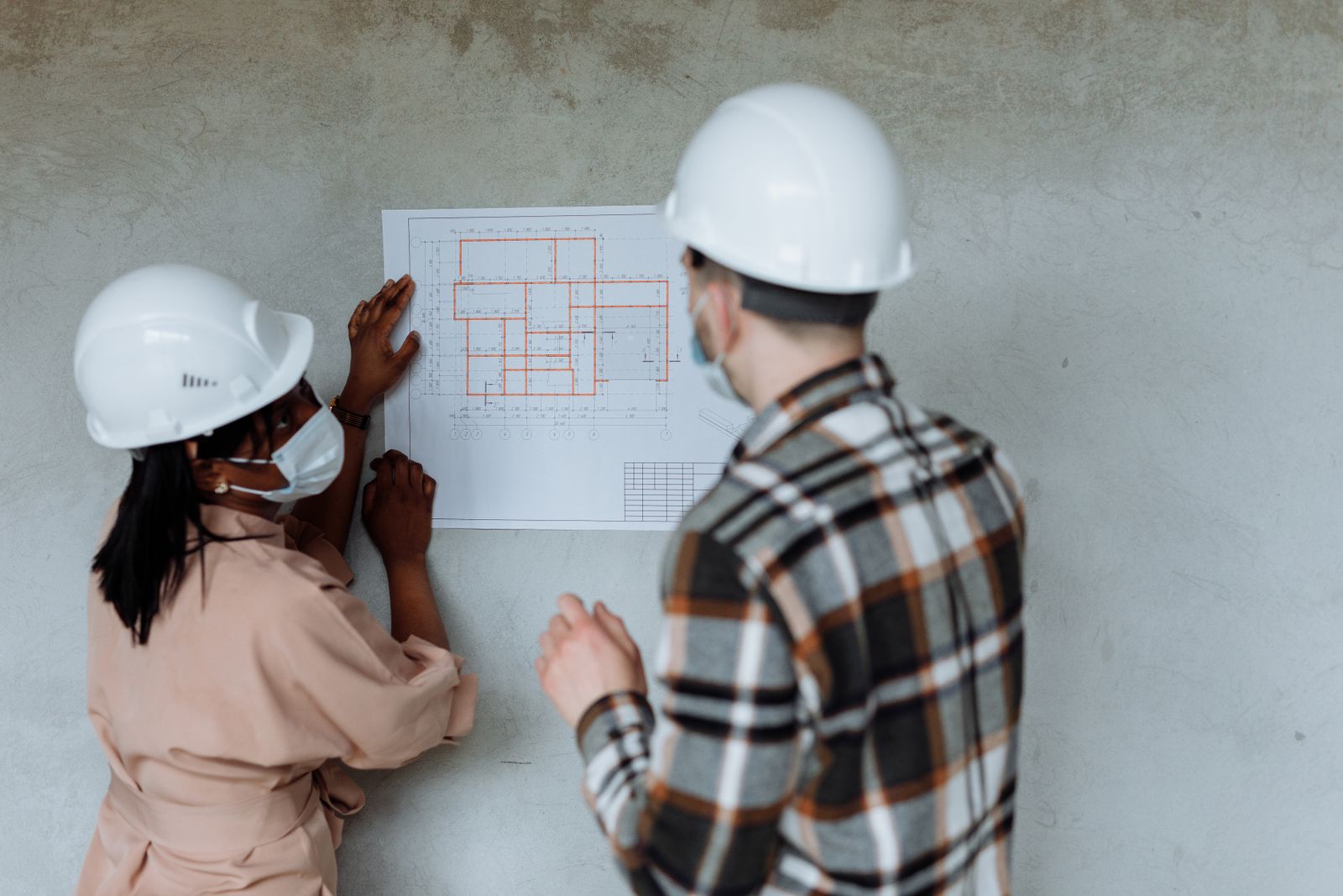 Planos de arquitectura desenrollados sobre una mesa de madera, junto a un casco de obra blanco