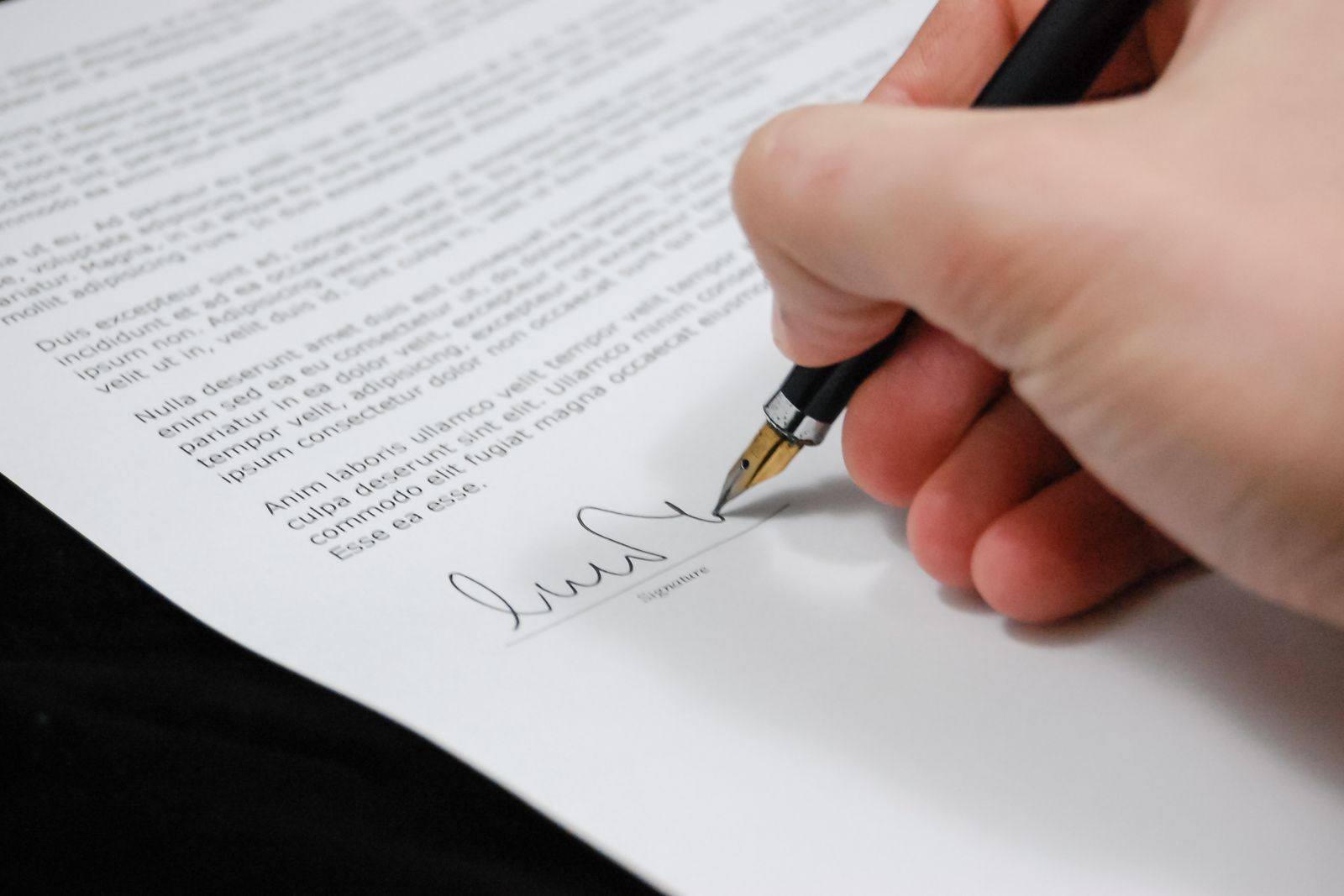 Detalle de una firma en un documento legal con un bolígrafo de tinta negra sobre un escritorio